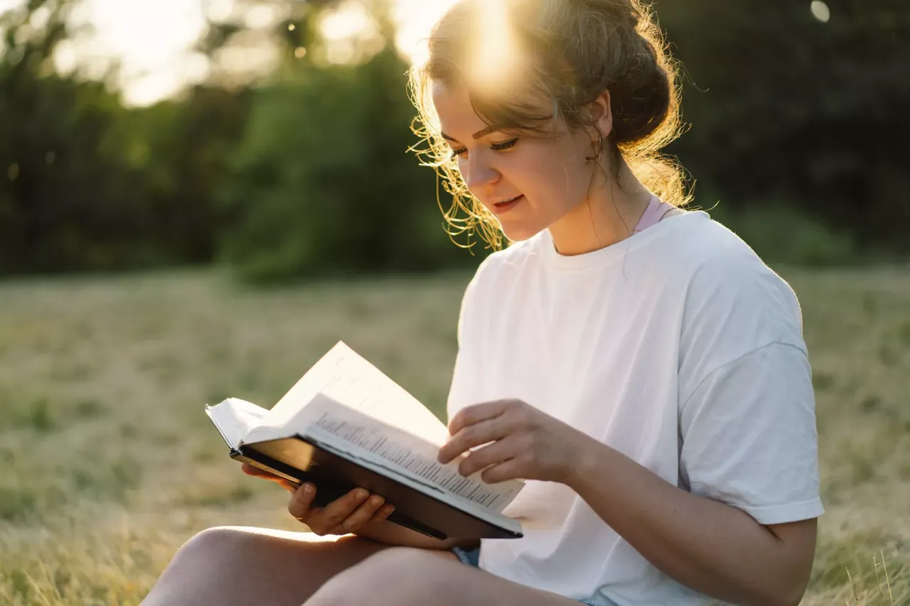 Person sitzt auf einer Wiese und liest die Bibel.