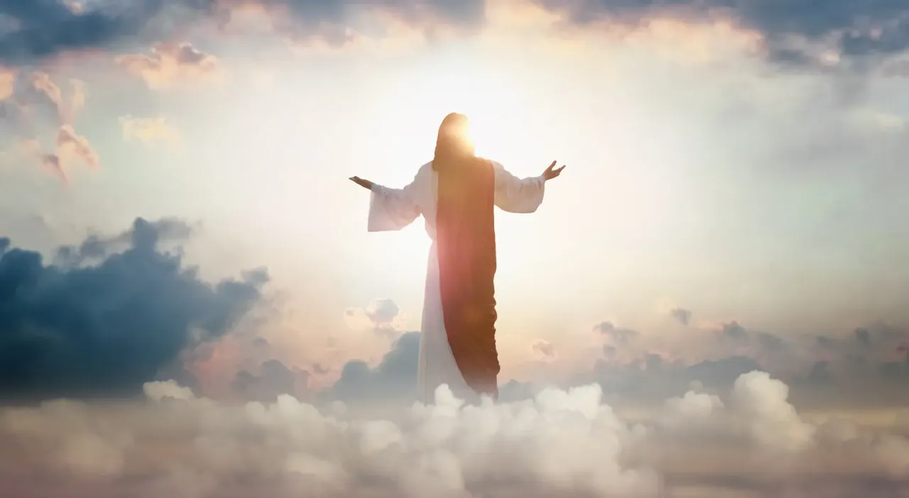 Der auferstandene Jesus Christus der mit erhobenen Hu00e4nden u00fcber dem hellen Lichthimmel und in den Wolken steht.