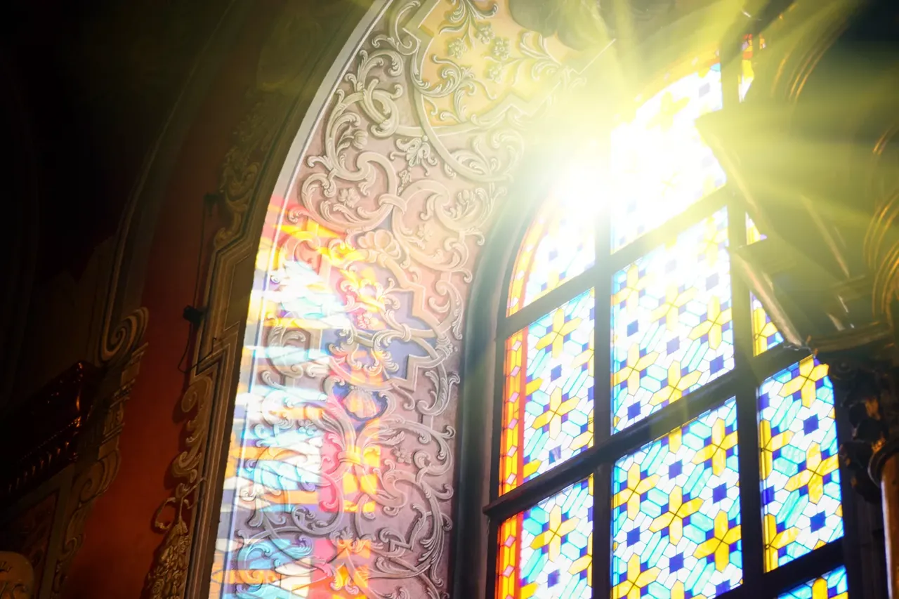 Eine Kirche von innen betrachtet mit buntem Fensterglas auf dem Fenster und hereinscheinenden Sonnenlicht von auu00dfen.